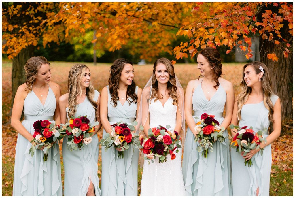 Bridesmaids laugh in front of a fall trees while in detroit michigan.