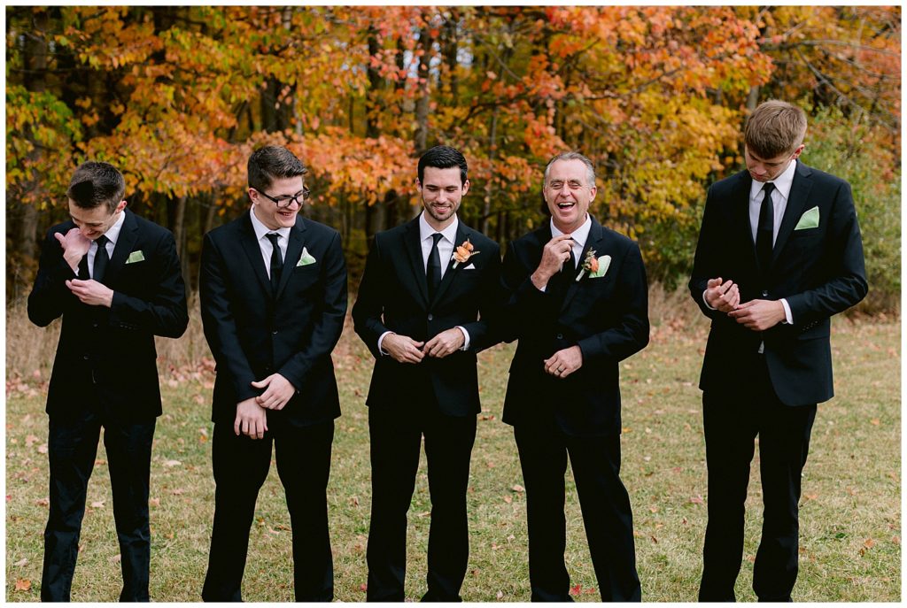 Groomsmen laugh while they fix their tuxes. Taken by luxury detroit wedding photographer Faith Rowley.