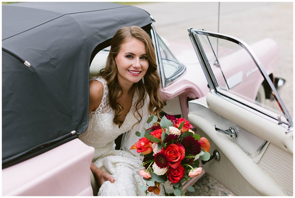 Bride in wedding dress getting out of classic get away thunderbird to her wedding ceremony. Luxury looking wedding photo taken in detroit michigan.