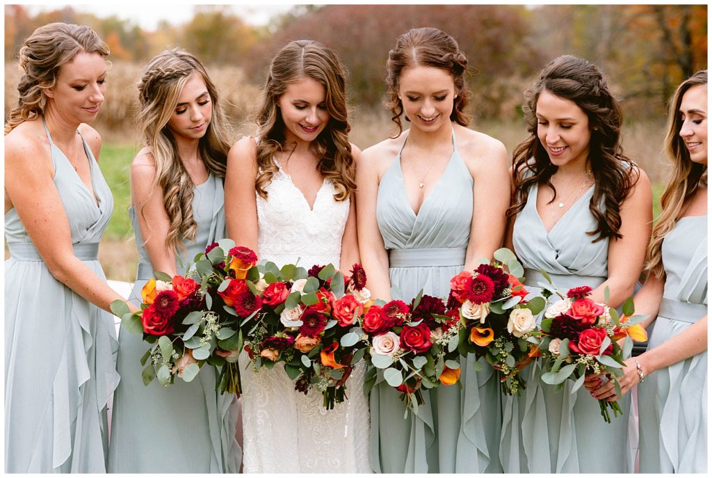 bridesmaid with flower bouquets huddle together for a photo in detroit michigan at a private residence at the reception