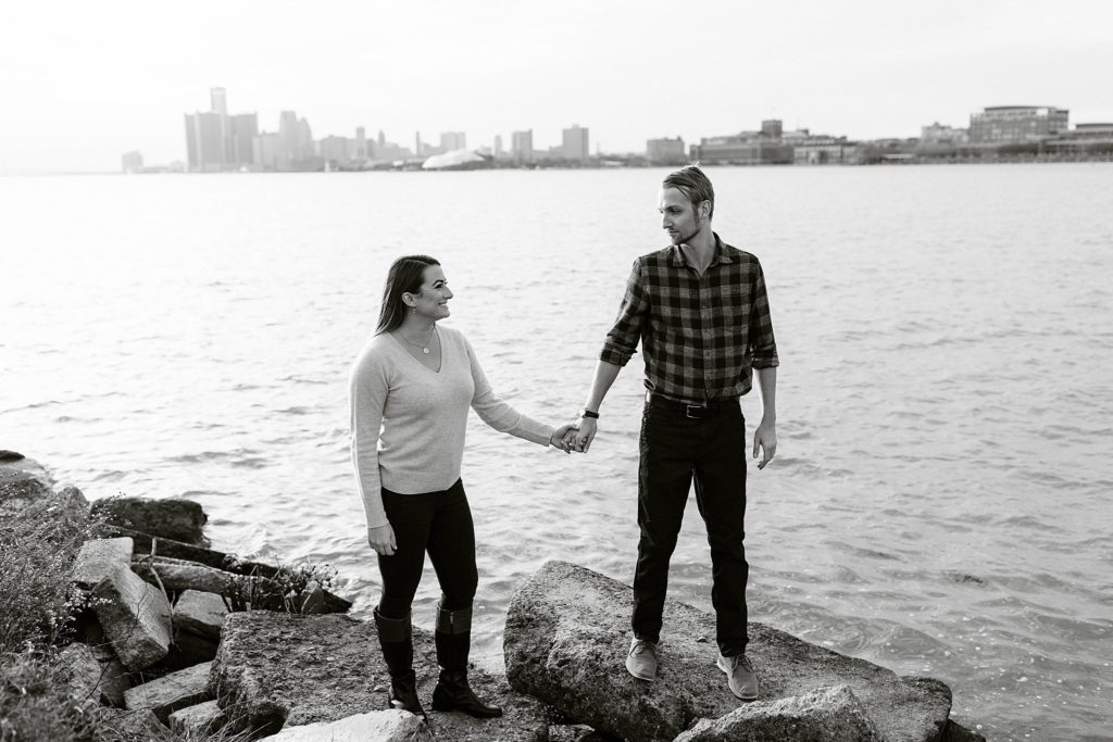belle isle engaged couple holds hand in front of city of detroit
